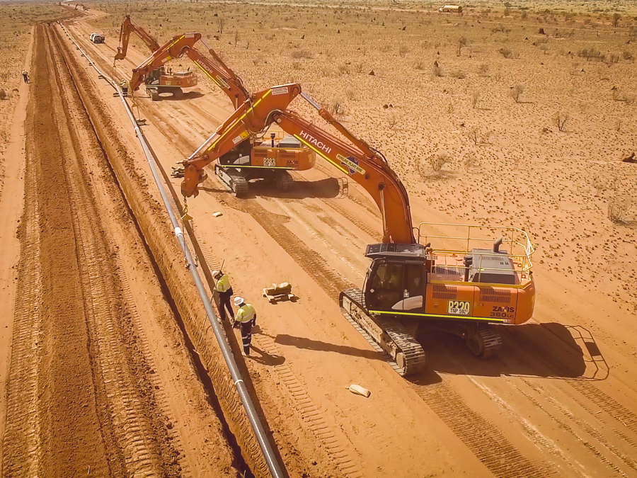 A series of excavators laying pipe into a trench in the outback.