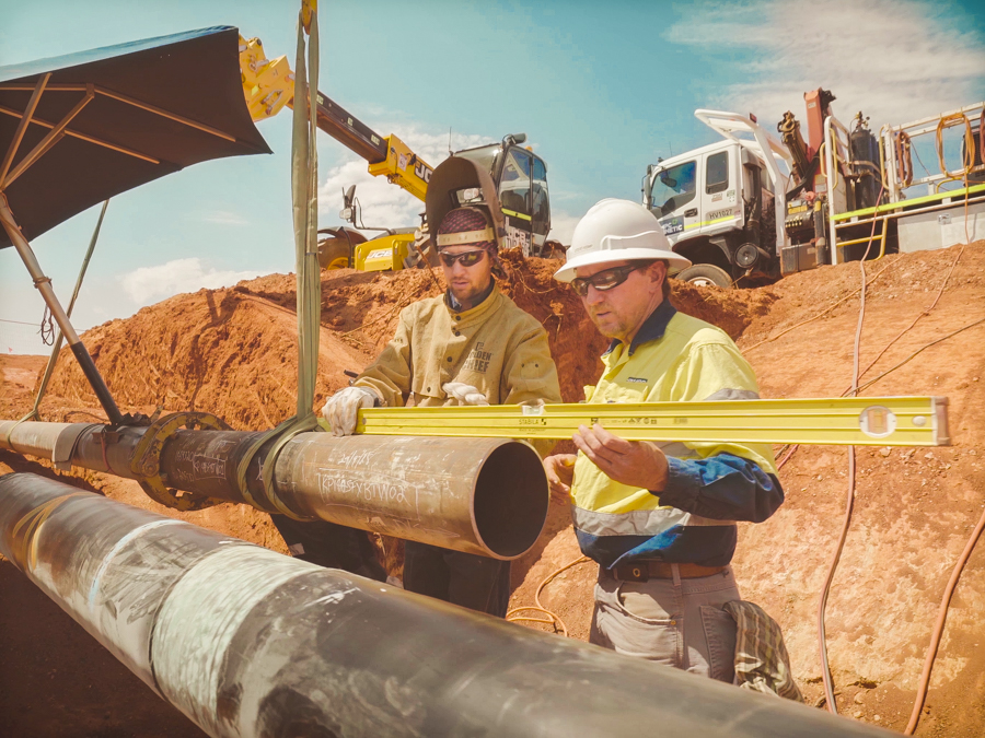 Workers measuring a pipe in a trench.